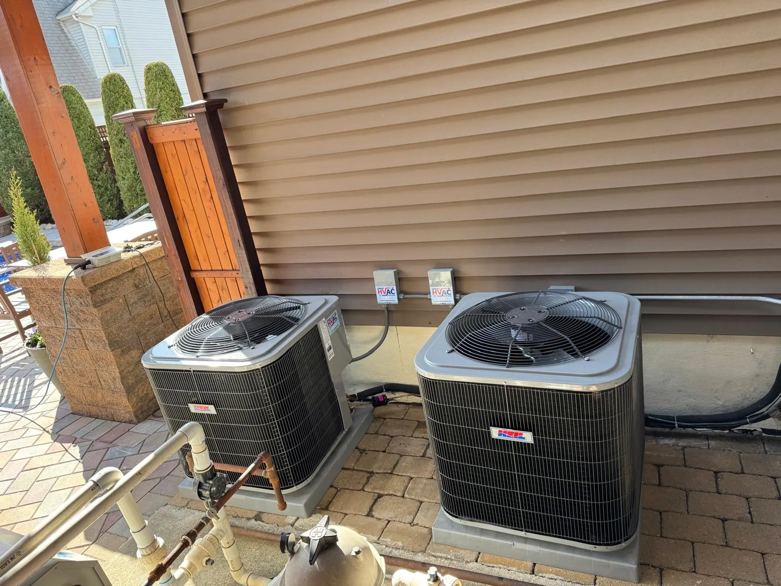 Two outdoor air conditioning condensers installed on pads beside a building with disconnect boxes and refrigerant lines